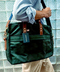 Person holding a green bag with a visible brand tag against a glass block wall.