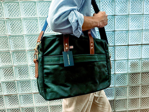 Person holding a green bag with a visible brand tag against a glass block wall.