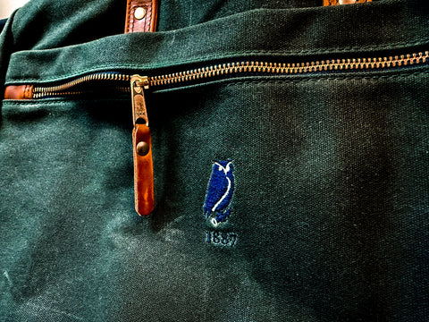 Close-up of a green bag with a zipper and a logo on a dark background