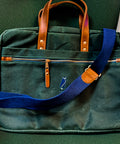 Green bag with blue strap and brown handles on a green chair