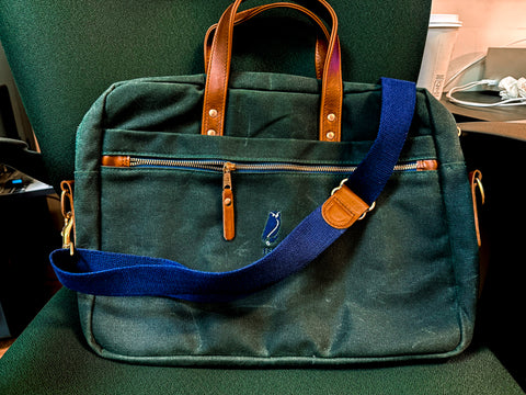 Green bag with blue strap and brown handles on a green chair